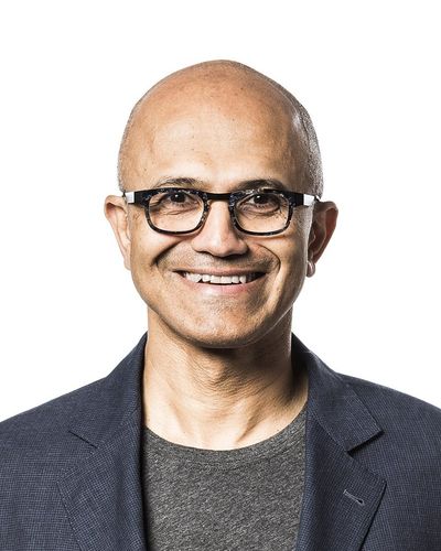 Satya Nadella smiling, in glasses and a dark jacket over a grey shirt