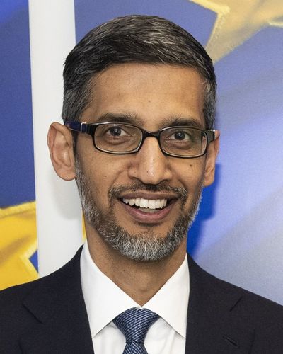 Sundar Pichai smiling, in glasses, a dark suit and tie