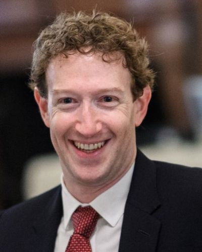 Mark Zuckerberg smiling, in a dark suit and red tie
