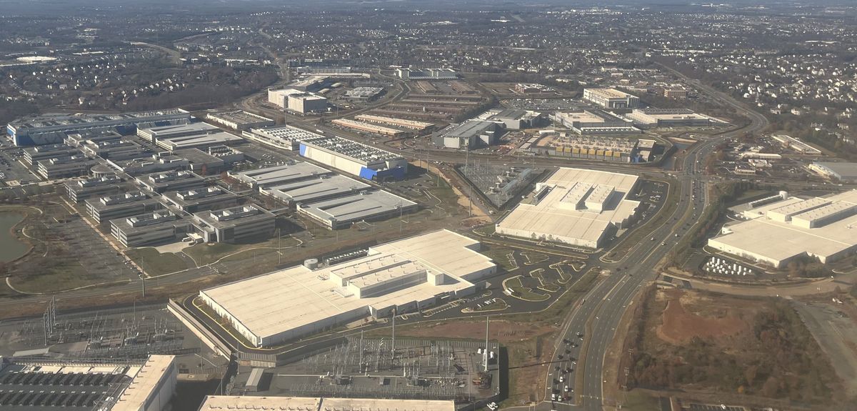 Aerial view of large flat-roofed data center buildings among roads, power substations and housing near Ashburn, Virginia