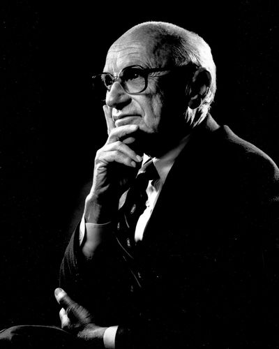 Black and white portrait of Milton Friedman, an older man in glasses and a suit, resting his chin on his hand